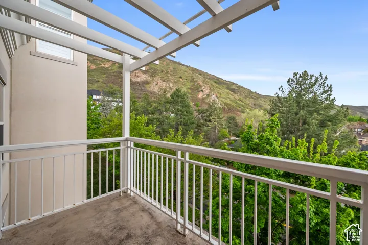 Private balcony with a slatted pergola, offering expansive mountain scenery and mature trees