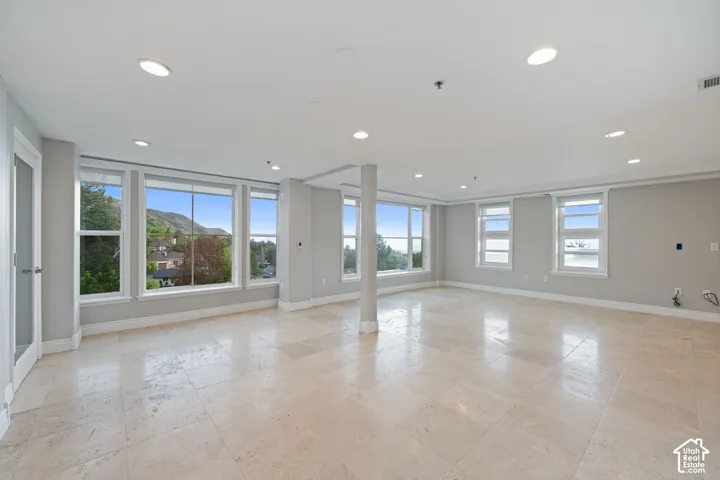 Expansive open-concept room featuring light-toned tile flooring, recessed lighting, multiple large windows, and a neutral wall palette