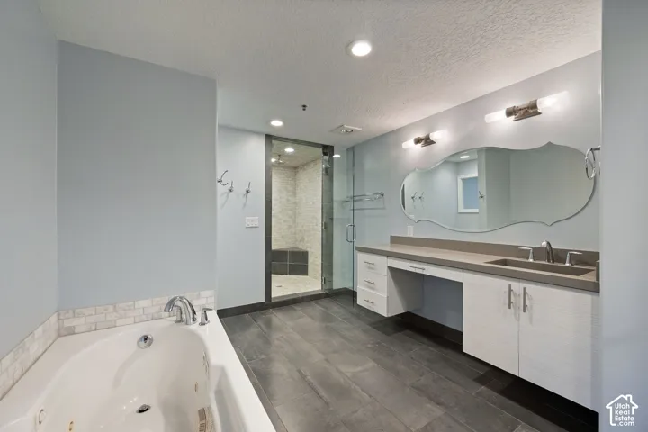 Spacious bath featuring wood-finish flooring, a soaking tub with tile surround, a walk-in shower with glass enclosure, a dual vanity with integrated sink, and an ornate mirror