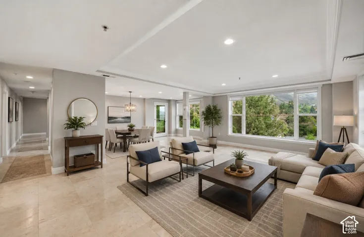 Recessed lighting illuminates the expansive living area with light-toned tile flooring, crown molding, and large windows