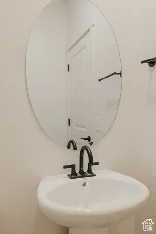 Pedestal sink with a matte black faucet, oval mirror, and neutral wall color