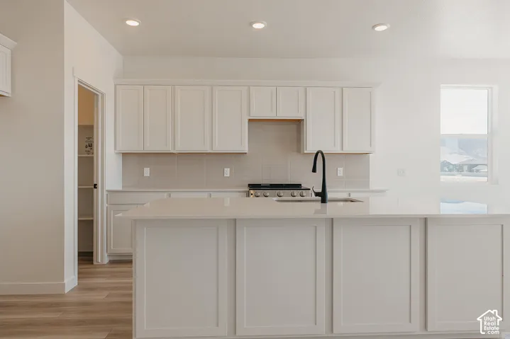 White shaker cabinetry, light-toned wood-finish flooring, recessed lighting, integrated range, and a built-in pantry