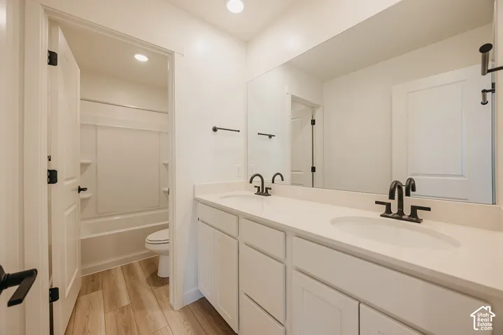 Double vanity with integrated sinks, light-toned countertop, matte black fixtures, and wood-finish flooring