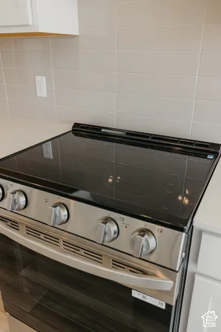 Modern electric range featuring a sleek black cooktop surface, stainless steel frame, and four control knobs with a backsplash of neutral subway tile and coordinating cabinetry above