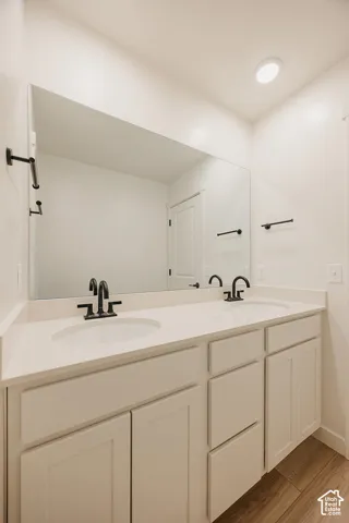Dual undermount sinks with matte black faucets, an expansive countertop, white shaker-style cabinetry, and wood-finish flooring