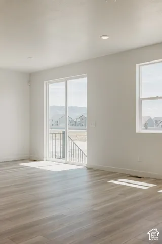 Sliding glass door leading to a balcony with metal railing, multiple windows, wood-finish flooring, and recessed ceiling lighting