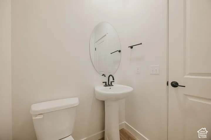 Pedestal sink with matte black faucet, oval mirror, and neutral wall paint