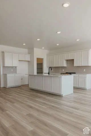 Kitchen featuring white shaker cabinetry, an island with a sink and matte black faucet, a light tile backsplash, and wood-finish flooring