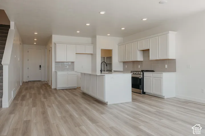 Open-concept kitchen featuring an island with a sink, white cabinetry, stainless steel appliances, and wood-finish flooring