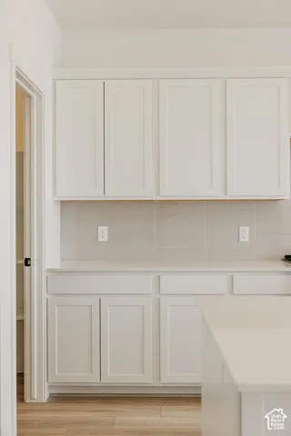 White shaker-style cabinetry, light-toned countertop surfaces, tile backsplash, and wood-finish flooring