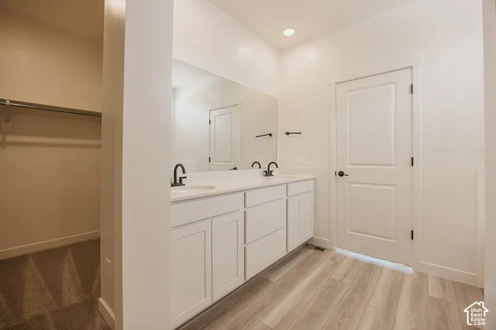 Dual vanity with integrated sinks, expansive mirror, wood-finish flooring, and recessed ceiling lighting