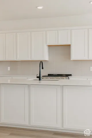 Recessed lighting, extensive white shaker cabinetry, light-toned countertops, tile backsplash, and a gas range
