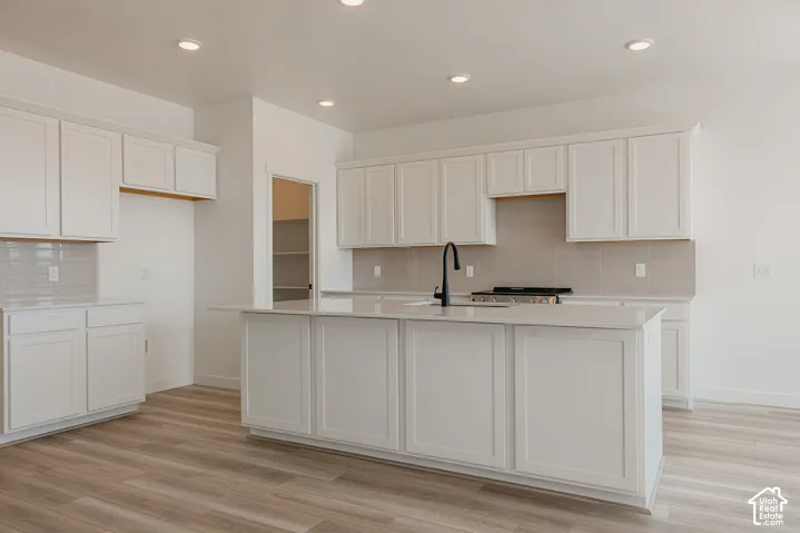 Kitchen featuring wood-finish flooring, white cabinetry, light-toned countertops, tile backsplash, and recessed lighting