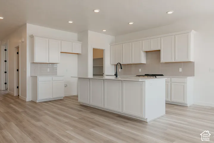 Modern kitchen featuring white shaker-style cabinetry, a large center island with waterfall countertop, stainless steel appliances including a gas cooktop, and wood-finish flooring throughout the open-concept space