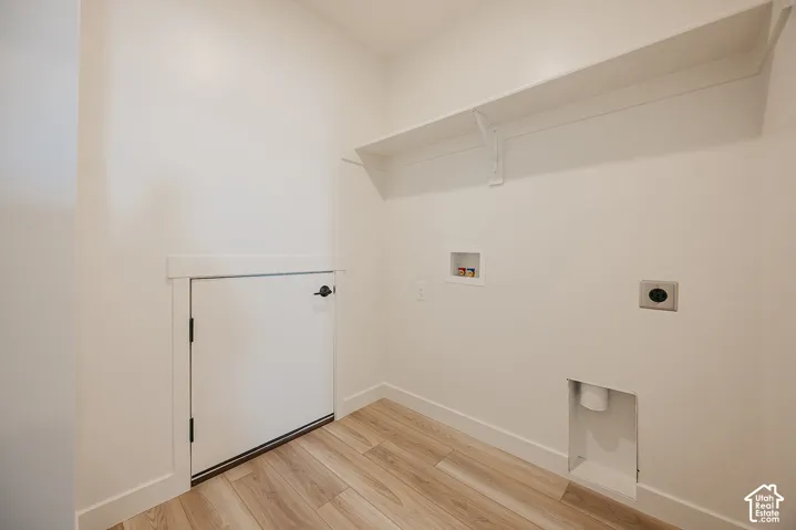 Laundry area featuring wood-finish flooring, white walls, built-in shelving, and a compact door with matte black hardware