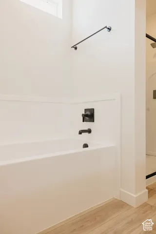 White soaking tub with matte black fixtures, wainscoting detailing, and light wood-finish flooring