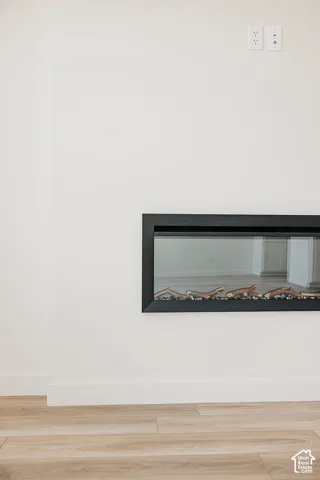 Modern linear electric fireplace with a black frame, light-toned wood-finish flooring, and crisp white walls