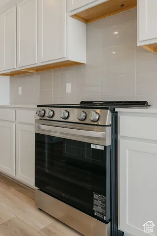 Stainless steel range and oven, white shaker-style cabinetry, wood-finish flooring, and light gray subway tile backsplash