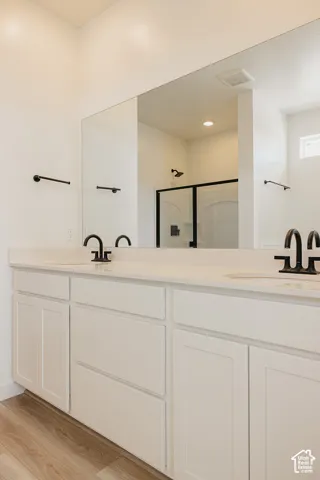 Dual vanity bathroom featuring a continuous quartz countertop, white cabinetry with shaker-style doors and drawers, matte black faucet fixtures, and a large framed mirror with integrated lighting
