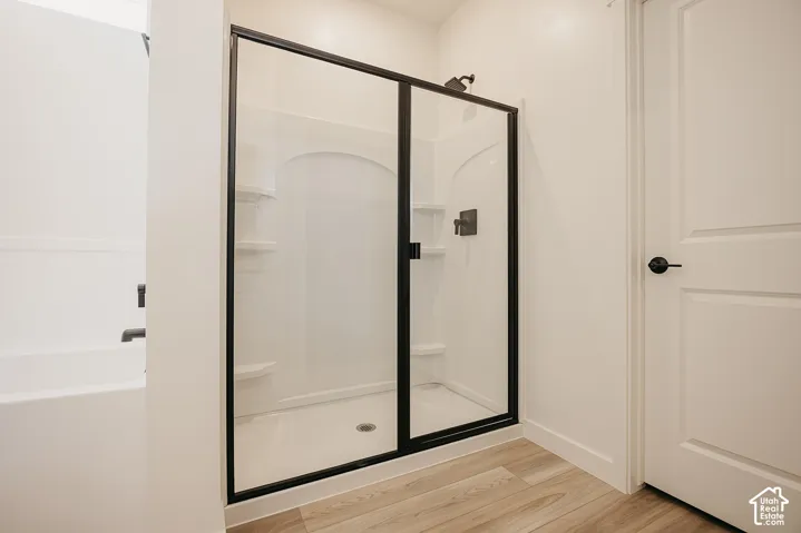 Shower enclosure with black framing and dark-finish fixtures, a built-in tub with a dark-finish faucet, and wood-finish flooring