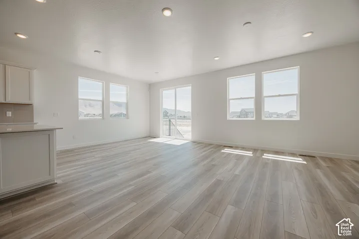 Spacious living area featuring wood-finish flooring, recessed lighting, multiple windows, and a sliding glass door to exterior