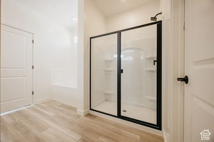 Spacious bathroom featuring wood-finish flooring, a white soaking tub, and a shower with black-framed glass doors and a matte black shower head