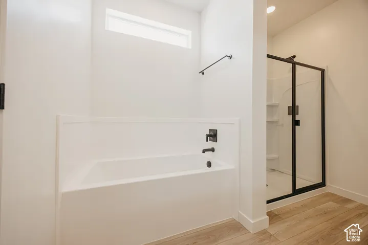 Soaking tub with matte black fixtures, separate shower with black-framed glass enclosure, and wood-finish flooring