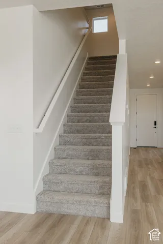 Carpeted staircase with a window, white handrail, and wood-finish flooring
