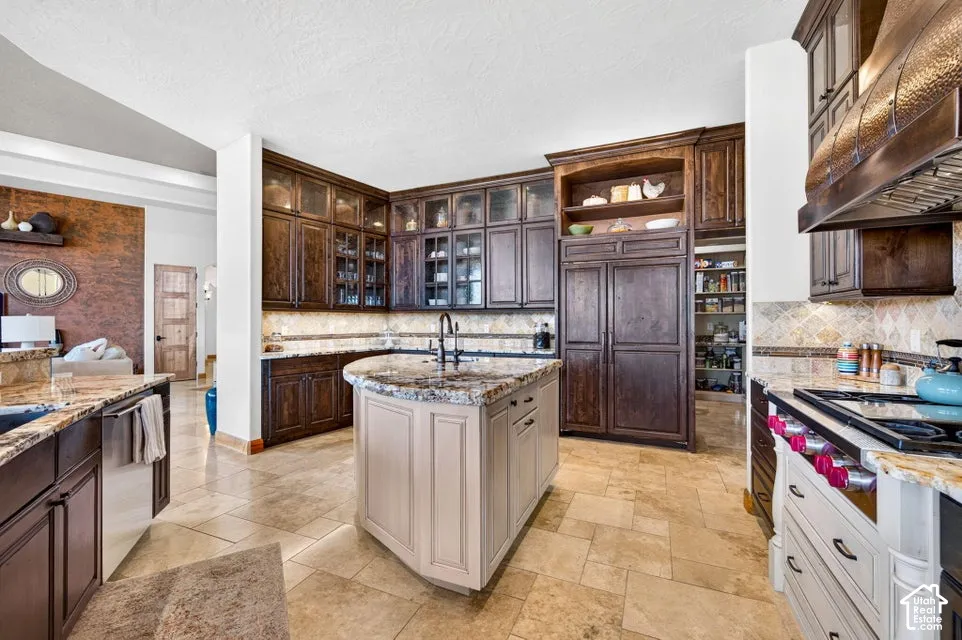 Gourmet kitchen featuring a large central island, dark wood-finish cabinetry, stone countertops, and tile flooring