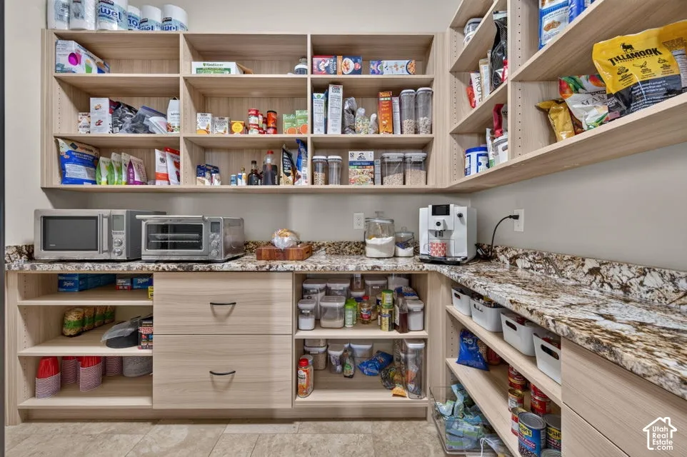 Extensive pantry featuring built-in light wood-finish shelving, substantial counter space with patterned stone-finish countertops, and integrated drawers with dark hardware