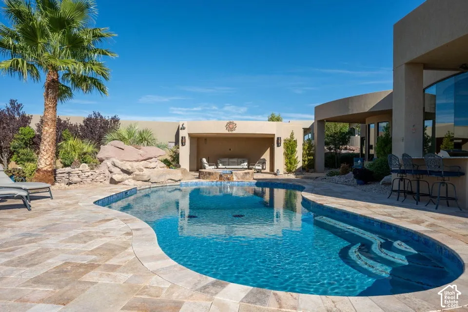 Resort-style backyard featuring a freeform swimming pool with integrated steps, an outdoor covered lounge area, and a built-in outdoor bar