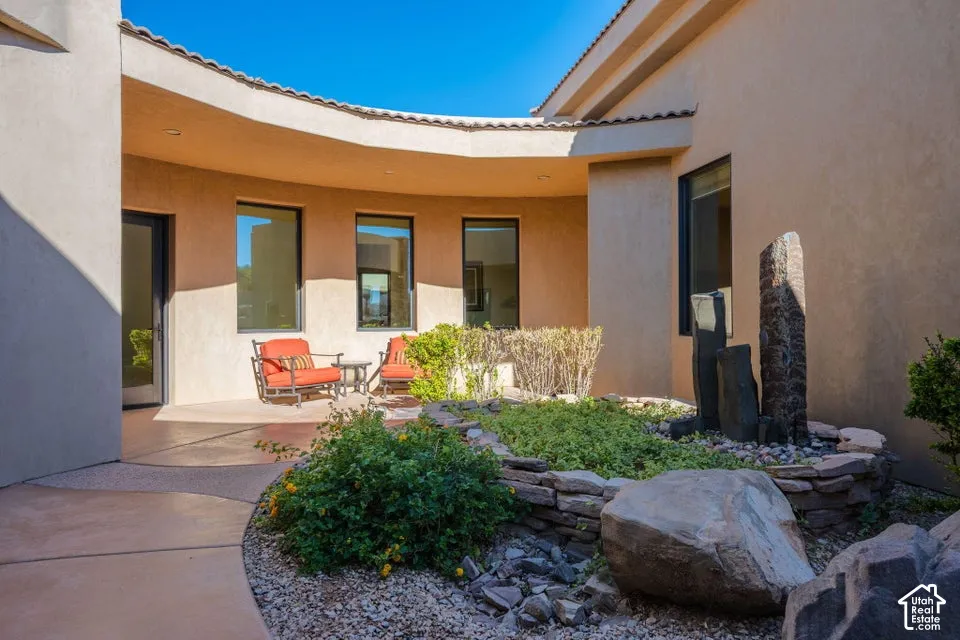 Curved stucco exterior with a tiled roofline, featuring a built-in rock garden with a stone water feature and established plantings