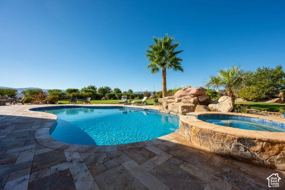 Curved swimming pool, stone tile patio, integrated spa, rock waterfall feature, and established palm trees