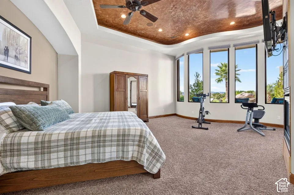 Recessed ceiling with an artistic finish, dark wood-finish ceiling fan, multiple tall windows, and wall-to-wall carpeting