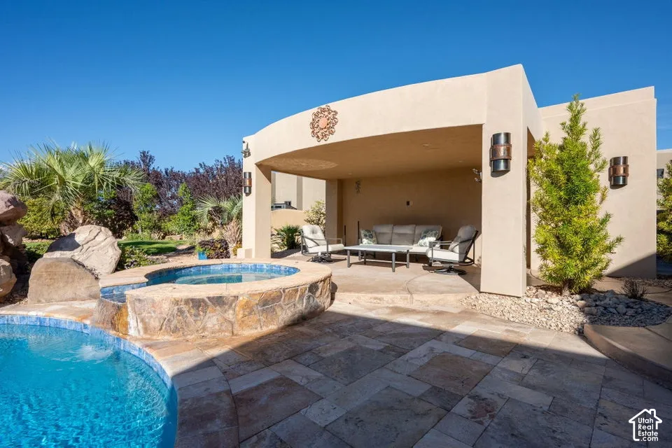 Outdoor living area featuring a stone-clad spa, swimming pool with water feature, covered patio, and extensive paved decking