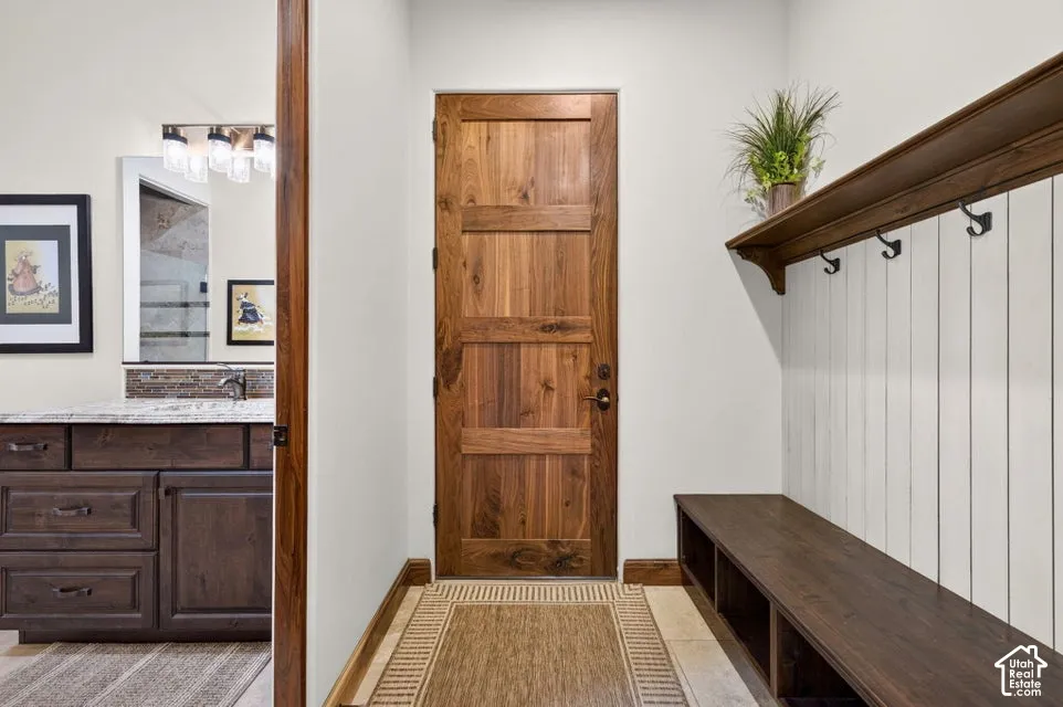Wood-paneled door, tile flooring, built-in mudroom bench with storage, coordinating wood shelf with hooks, and a bathroom vanity with a countertop and undermount sink