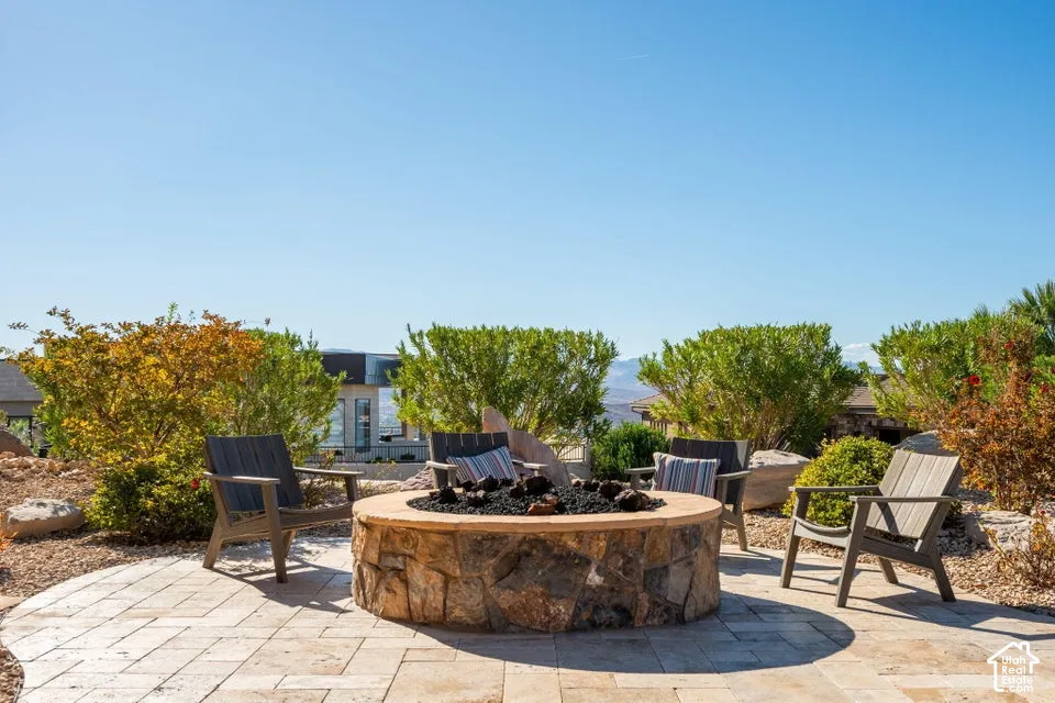Paver patio featuring a stone fire pit with black lava rock, surrounded by mature desert landscaping