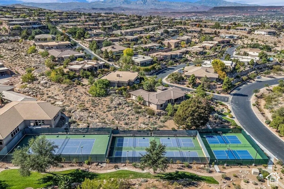 Community with multiple tennis courts, surrounding residential properties, and distant mountainous terrain