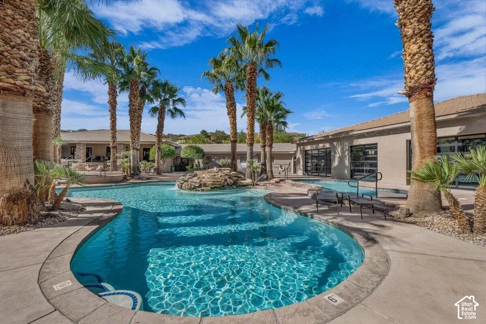Resort-style pool with integrated spa and rock waterfall feature, surrounded by mature palm trees and concrete decking