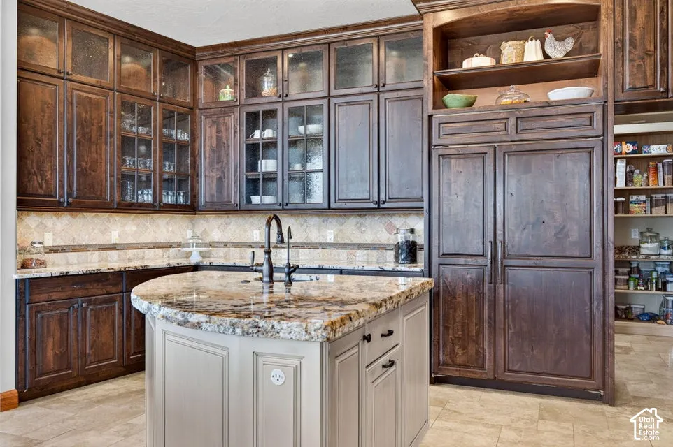 Kitchen featuring an island with stone countertop, dark wood-finish cabinetry, integrated paneled refrigerator, and tiled flooring