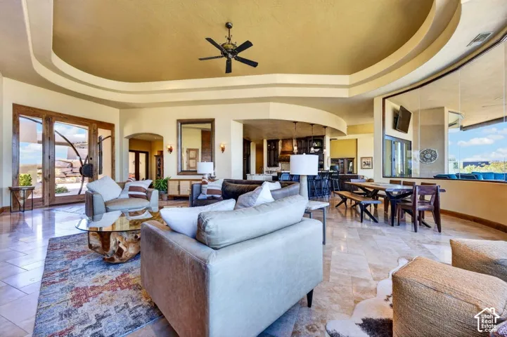 Spacious open-concept living area featuring a tray ceiling with a ceiling fan, large glass doors, an archway, and tiled flooring