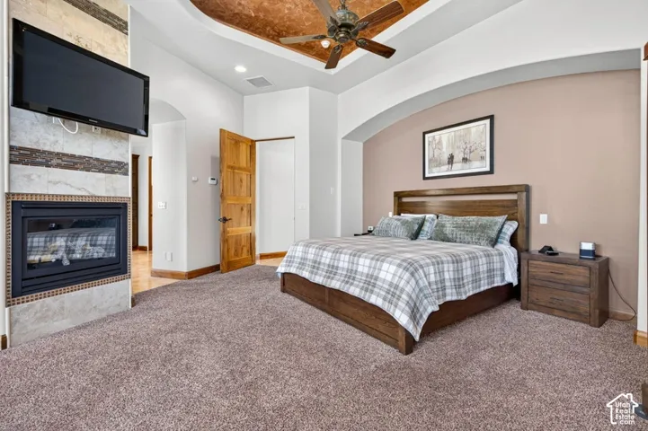 Recessed ceiling with wood-finish paneling and ceiling fan, built-in fireplace with stone-finish surround, wood-finish flooring, wood-finish door, and arched wall feature
