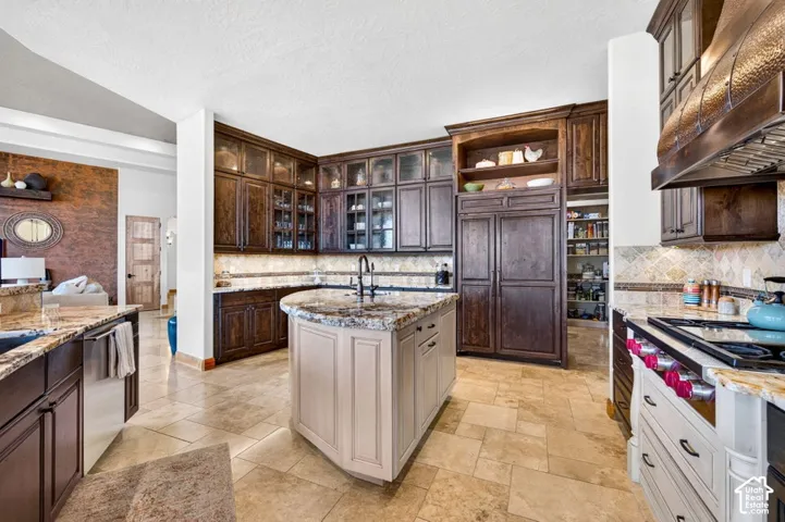 Gourmet kitchen featuring a large central island, dark wood-finish cabinetry, stone countertops, and tile flooring
