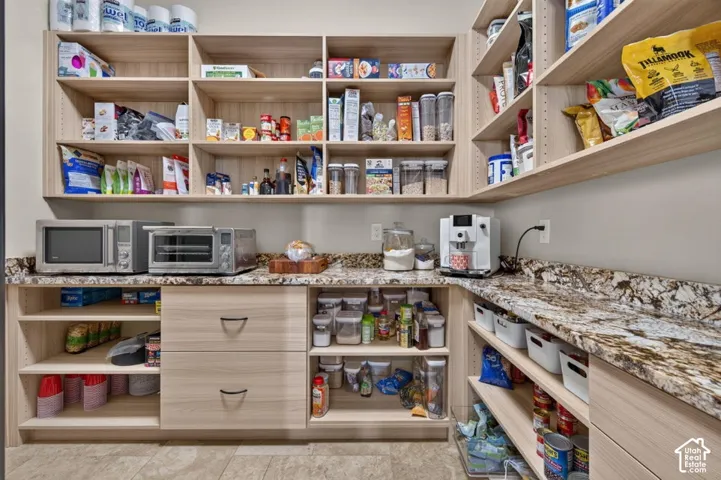 Extensive pantry featuring built-in light wood-finish shelving, substantial counter space with patterned stone-finish countertops, and integrated drawers with dark hardware