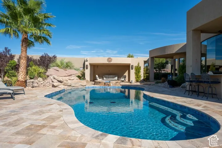 Resort-style backyard featuring a freeform swimming pool with integrated steps, an outdoor covered lounge area, and a built-in outdoor bar