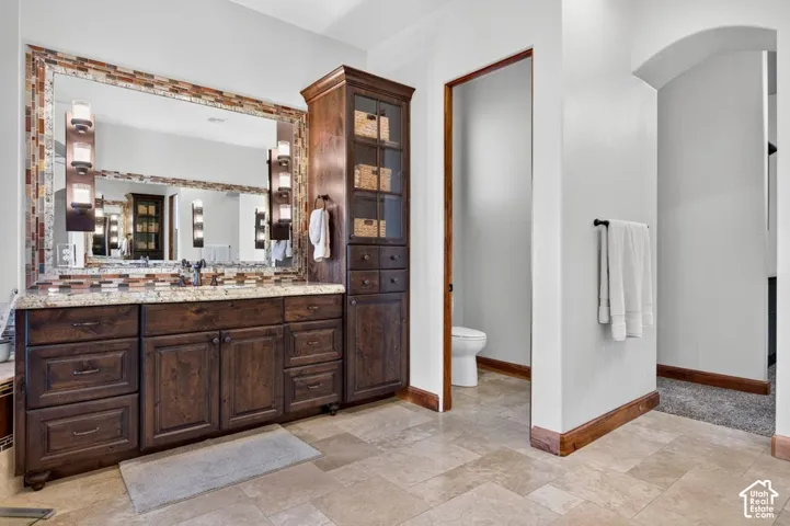 Dual vanity with rich wood cabinetry, integrated storage tower, expansive mirror with mosaic tile surround, and light-toned tile flooring
