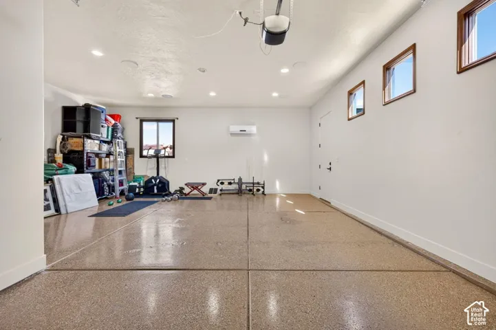 Epoxy flooring, recessed lighting, mini-split air conditioning unit, white walls, and multiple windows with dark wood trim
