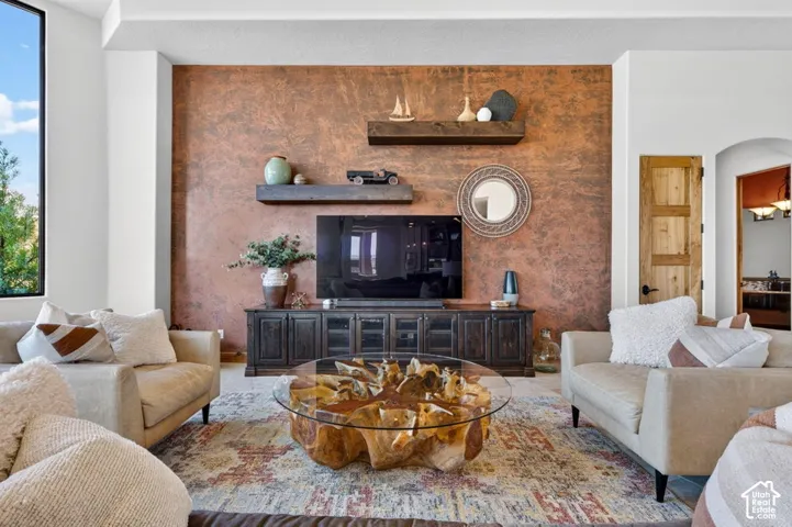 Accent wall with a textured finish, recessed lighting, built-in media console, wood floating shelves, and an arched doorway