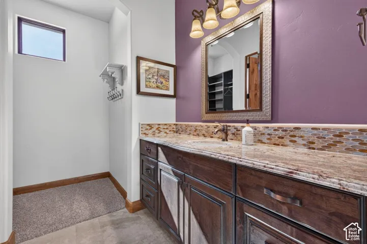 Wood-finish vanity with an integrated sink, granite-style countertop, mosaic tile backsplash, and decorative wall-mounted mirror