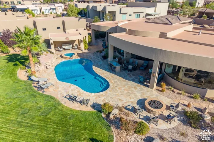 Resort-style backyard oasis featuring a freeform saltwater pool with sun shelf, expansive patio with integrated fire pit seating area, mature landscaping with specimen palms, and manicured lawn